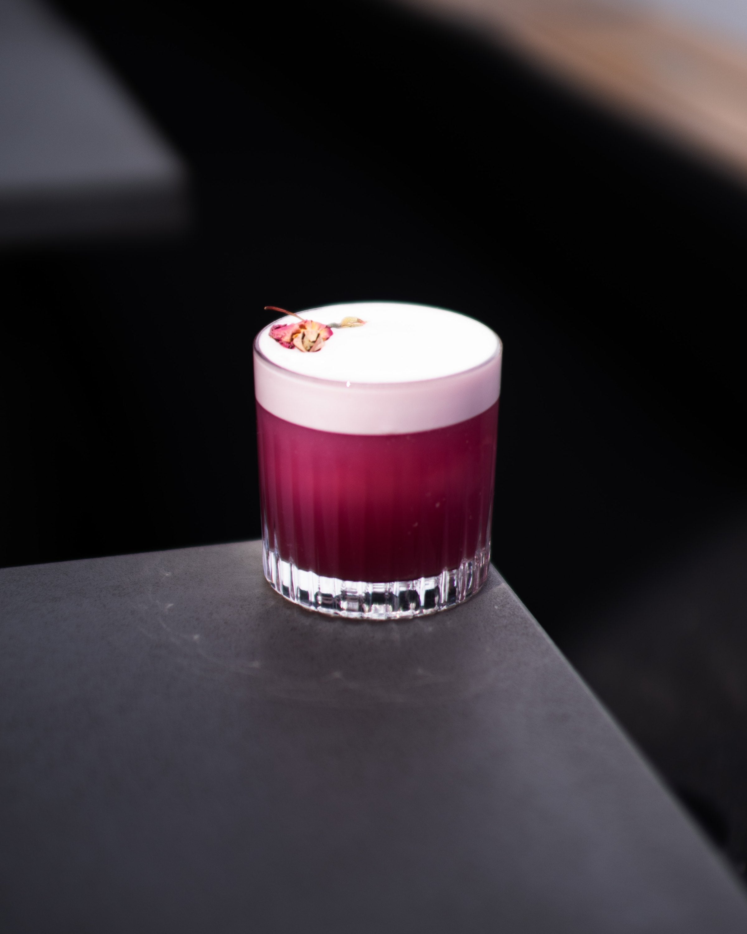 A cocktail garnished with a dried rose on the bar